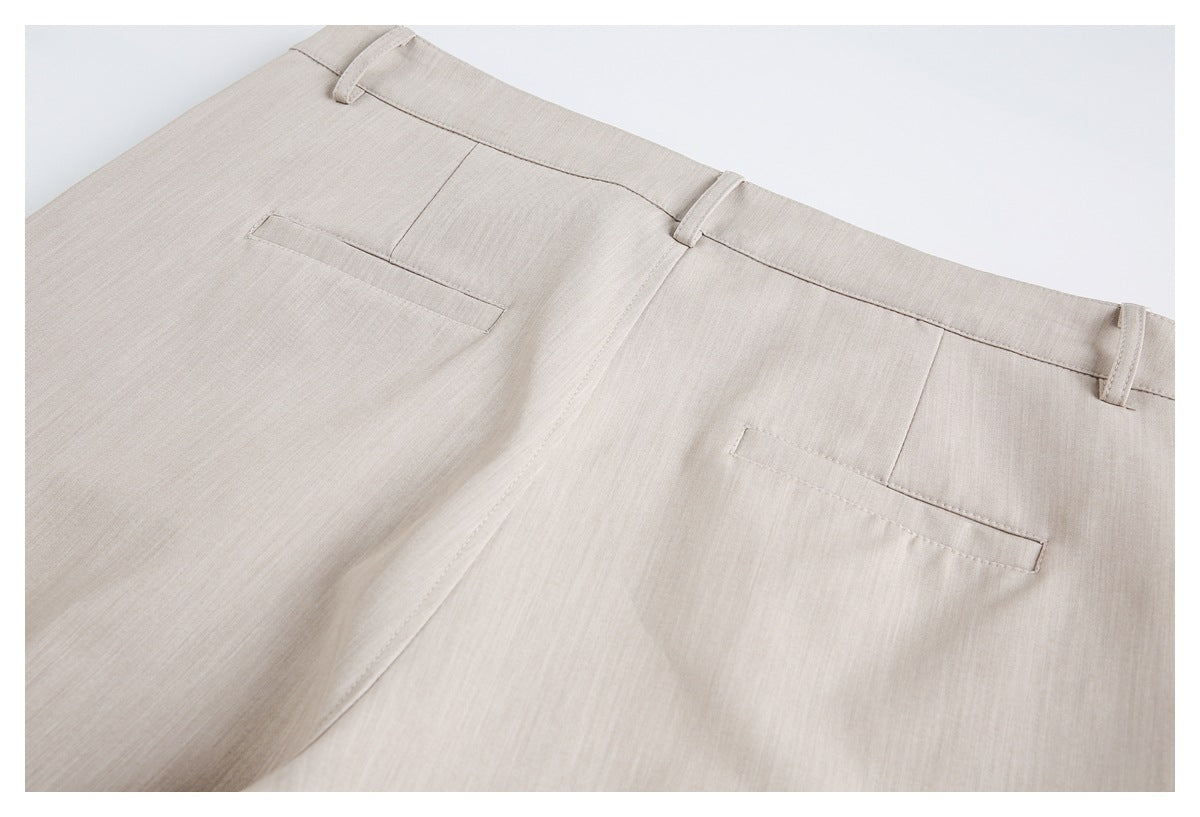 Cropped back view of beige trousers laid flat, showing the waistband, belt loops, and two welt pockets.