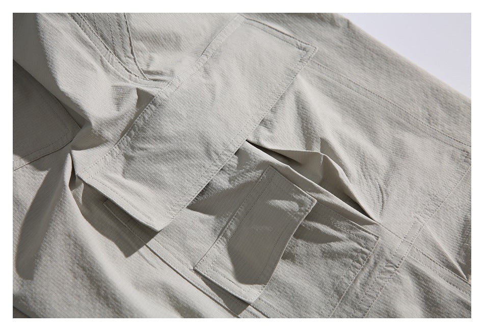 Close-up of a light gray garment with a broad stitched flap above a smaller rectangular pocket.