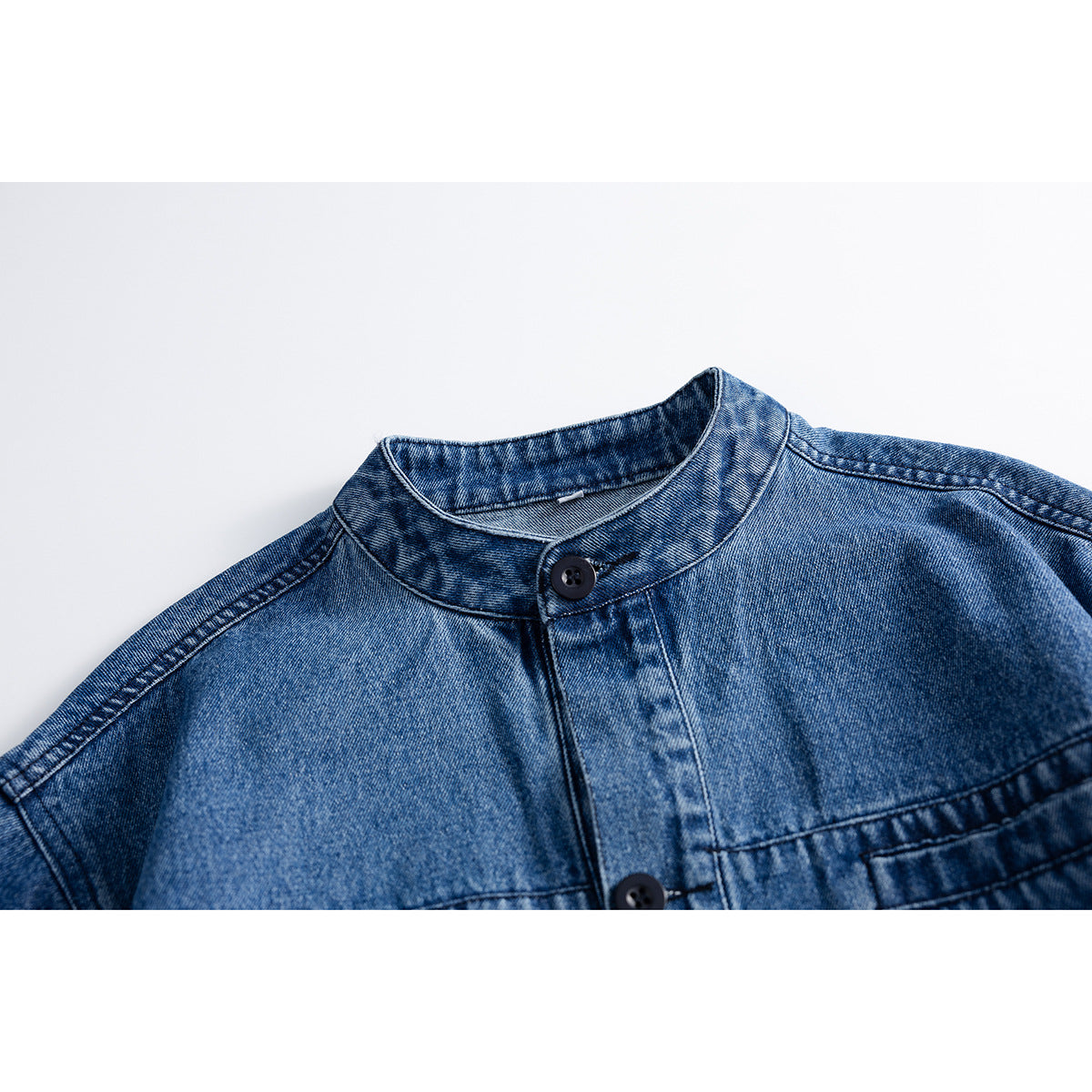 Close-up of a blue denim jacket's stand collar, front placket, and dark buttons.