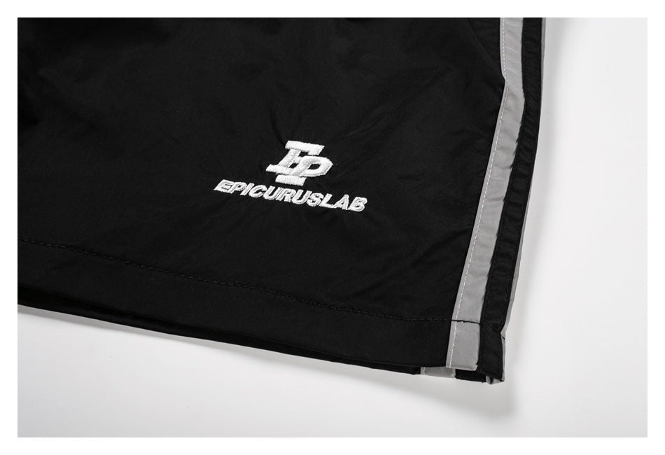 Close-up of black shorts with white embroidered lettering and a gray side stripe.