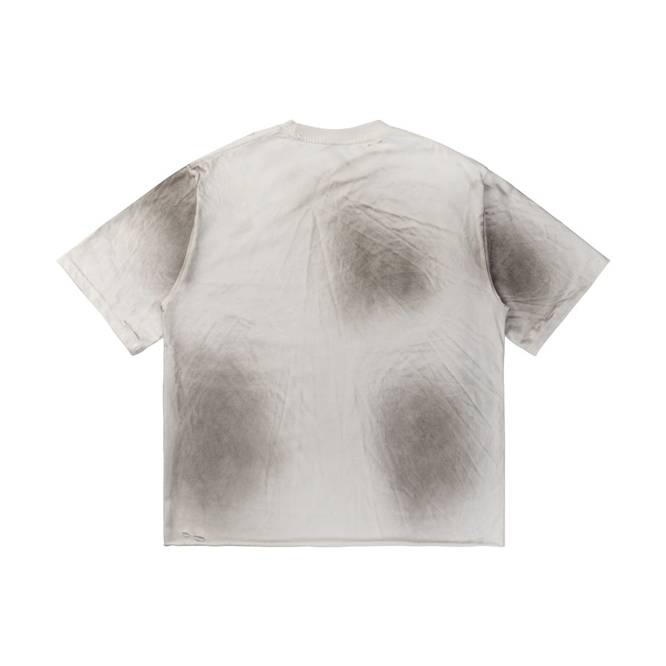 Back view of off-white T-shirt with gray spray smudges and small distressed slits at the hem and sleeves