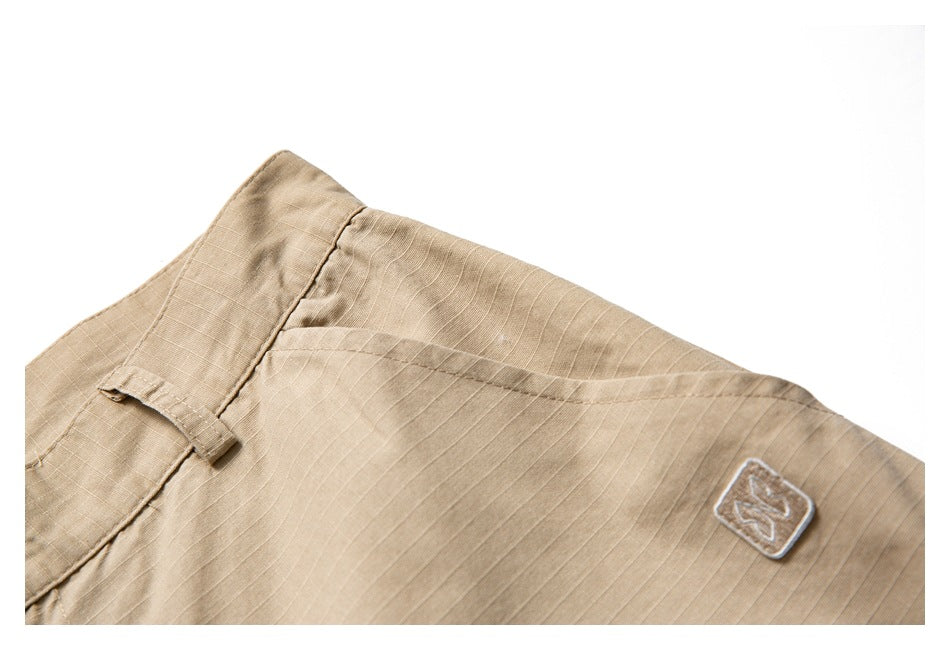 Close-up of tan ripstop garment fabric with a belt loop and a small embroidered square patch.