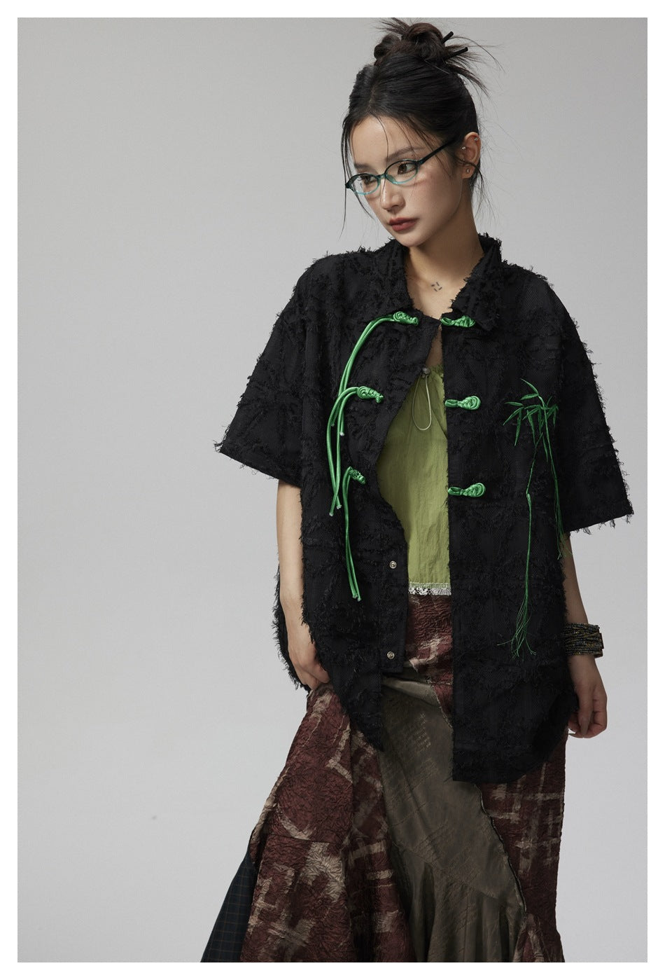 Model wearing a black textured short-sleeve jacket with green frog closures and bamboo embroidery.