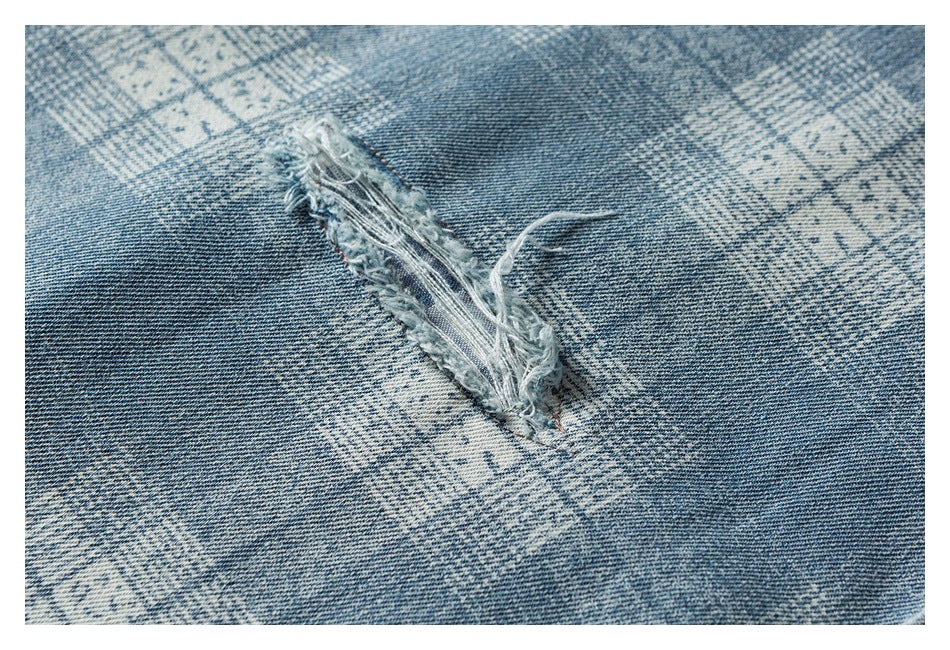Close-up of a long frayed tear in blue-gray patterned denim.