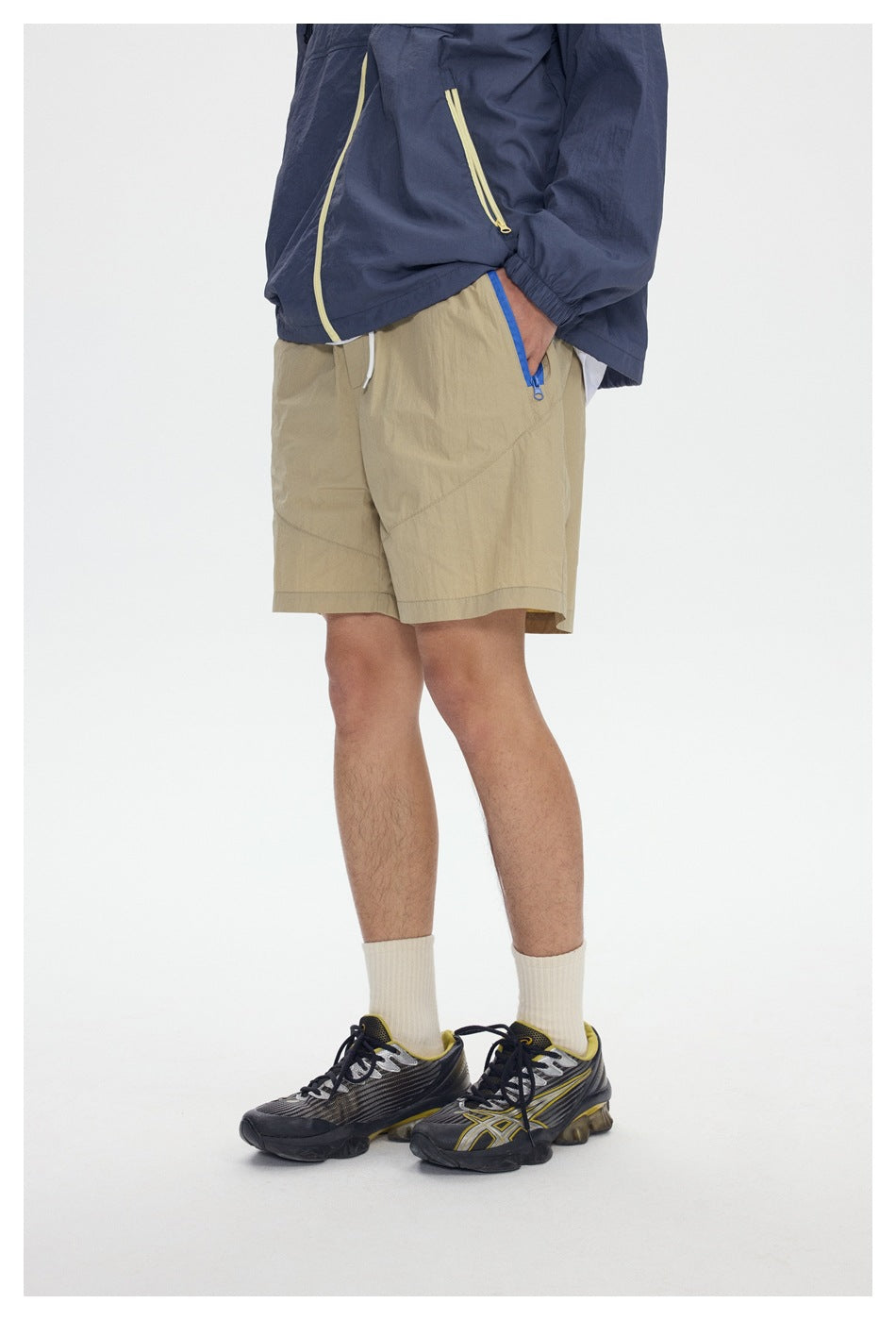 Angled close view of beige shorts with a blue zippered pocket, worn with a navy jacket.