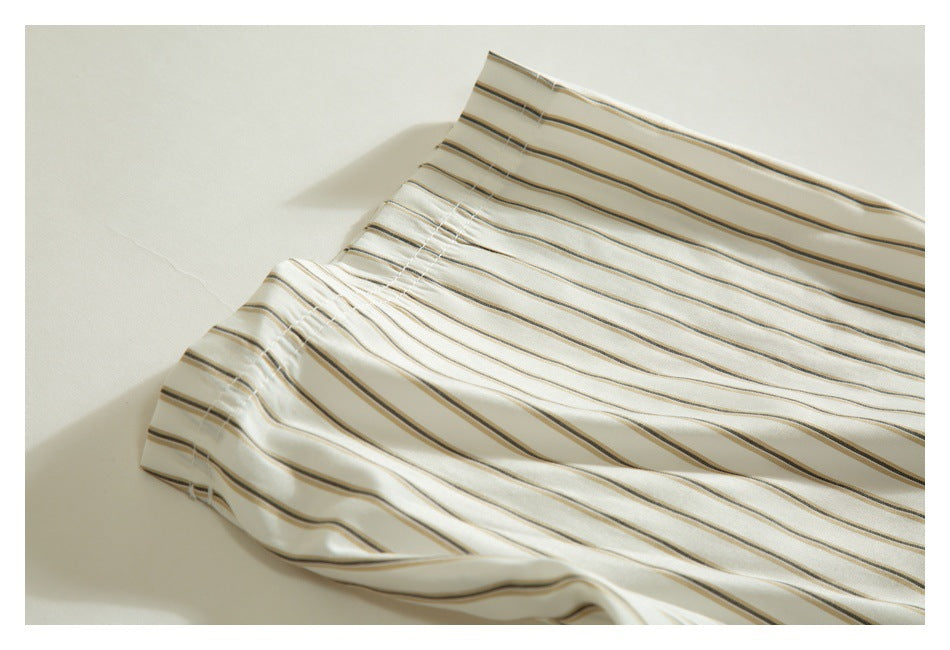 Close-up of cream fabric with thin brown and gray stripes, showing a folded, stitched edge.