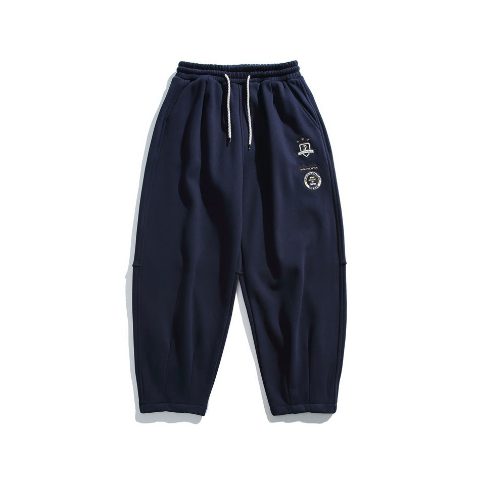 Navy sweatpants flat lay with drawstring waist, side pockets and embroidered badges on the left leg
