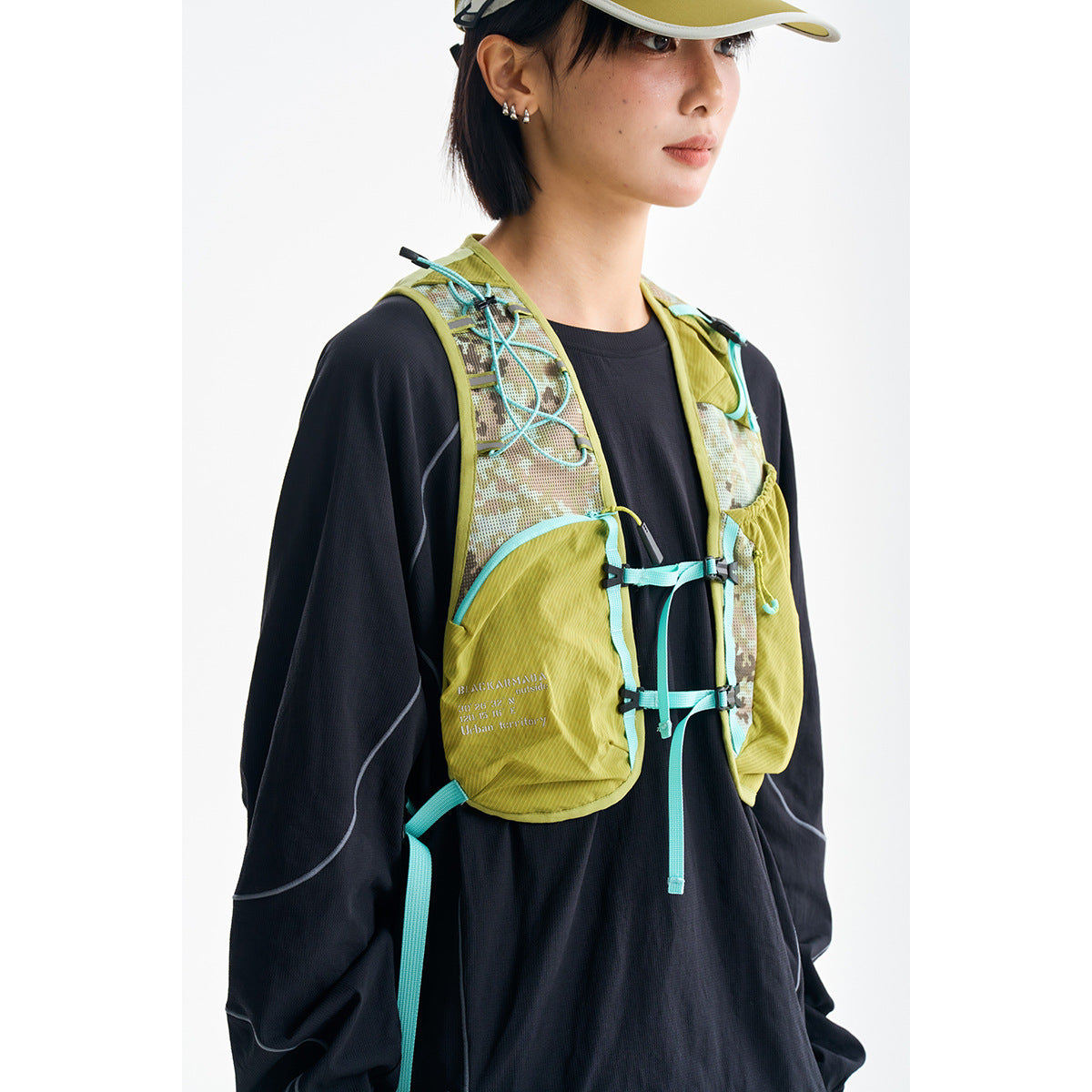 Close front view of a model wearing a lime-green and mesh running vest with turquoise cords over a black top.
