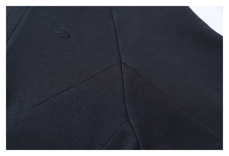 Close-up of curved panel seams and a small tonal embroidered emblem on dark navy fabric.