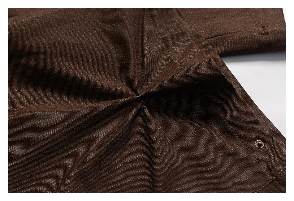 Close-up of brown trousers showing gathered folds, stitched seams, and a small metal snap.
