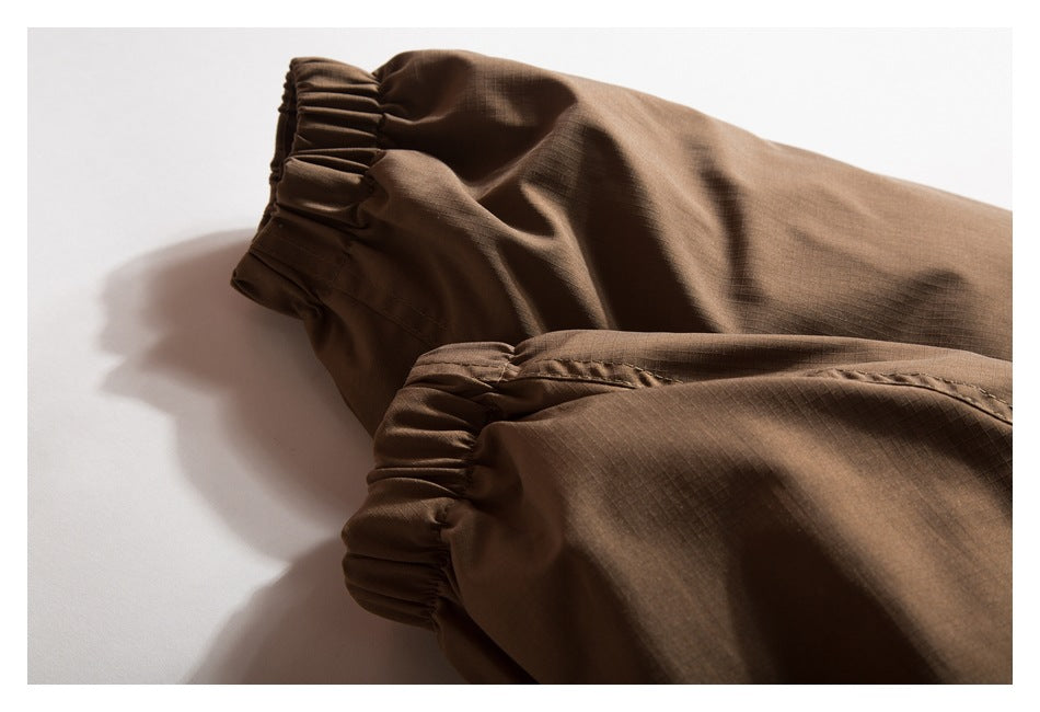 Close-up of two elasticized hems on brown garment legs against a white background.