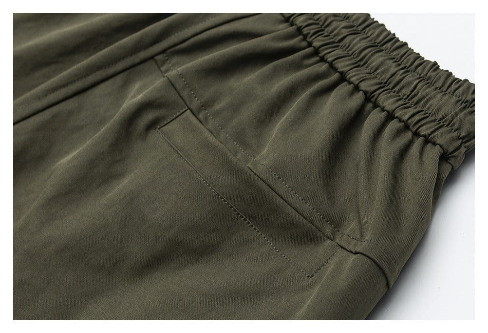 Close-up of olive trousers with a slanted pocket, visible stitching, and gathered elastic waistband.