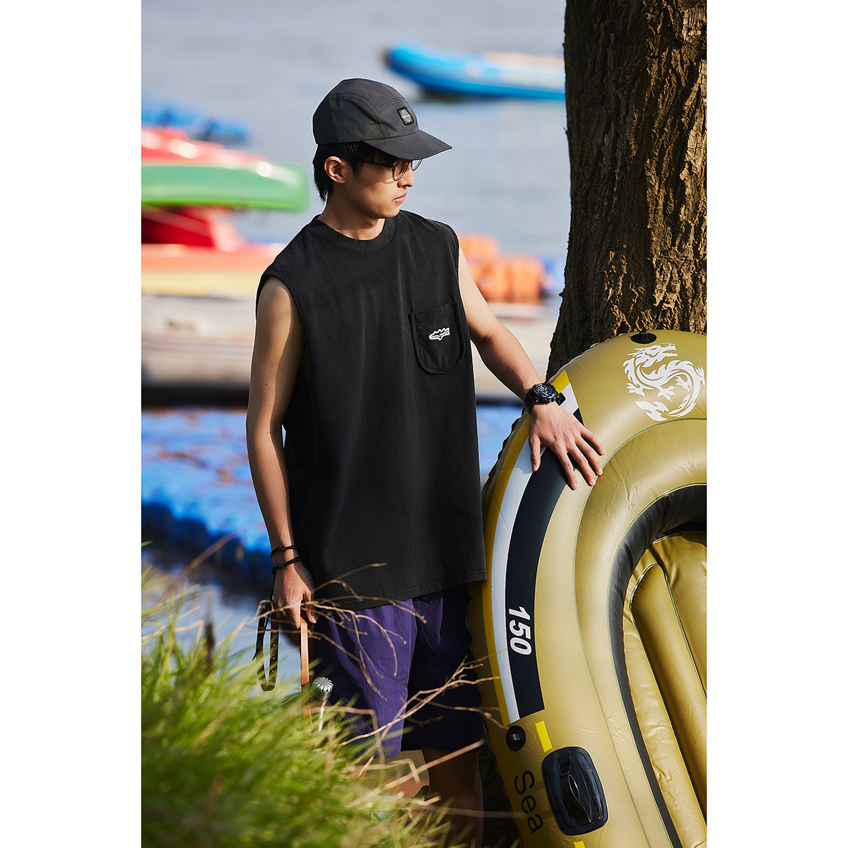 Model in a black sleeveless pocket shirt and purple shorts, standing beside a yellow inflatable ring.