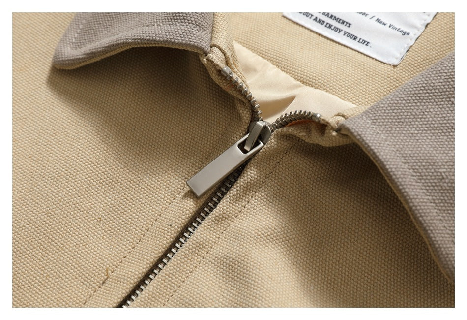 Close-up of a beige garment's metal zipper, contrasting collar edges, and partial inner label.