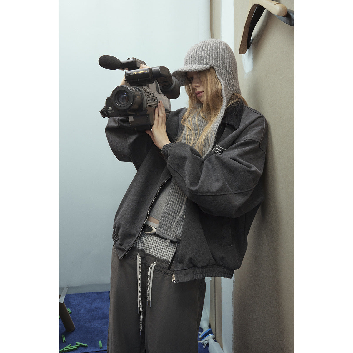 Model wearing a charcoal oversized zip jacket, gray knit hood and sweater, and dark drawstring pants while holding a video