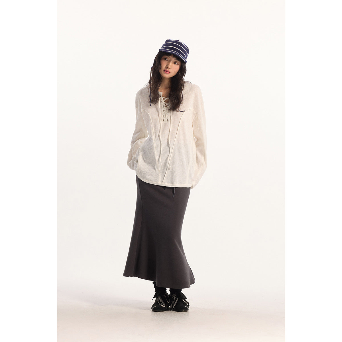 Full-length model wearing an ivory lace-up top, charcoal maxi skirt and navy striped bucket hat.