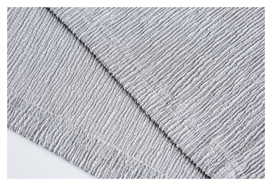 Close-up of the light gray textured shirt's stitched hem and overlapping fabric edge.