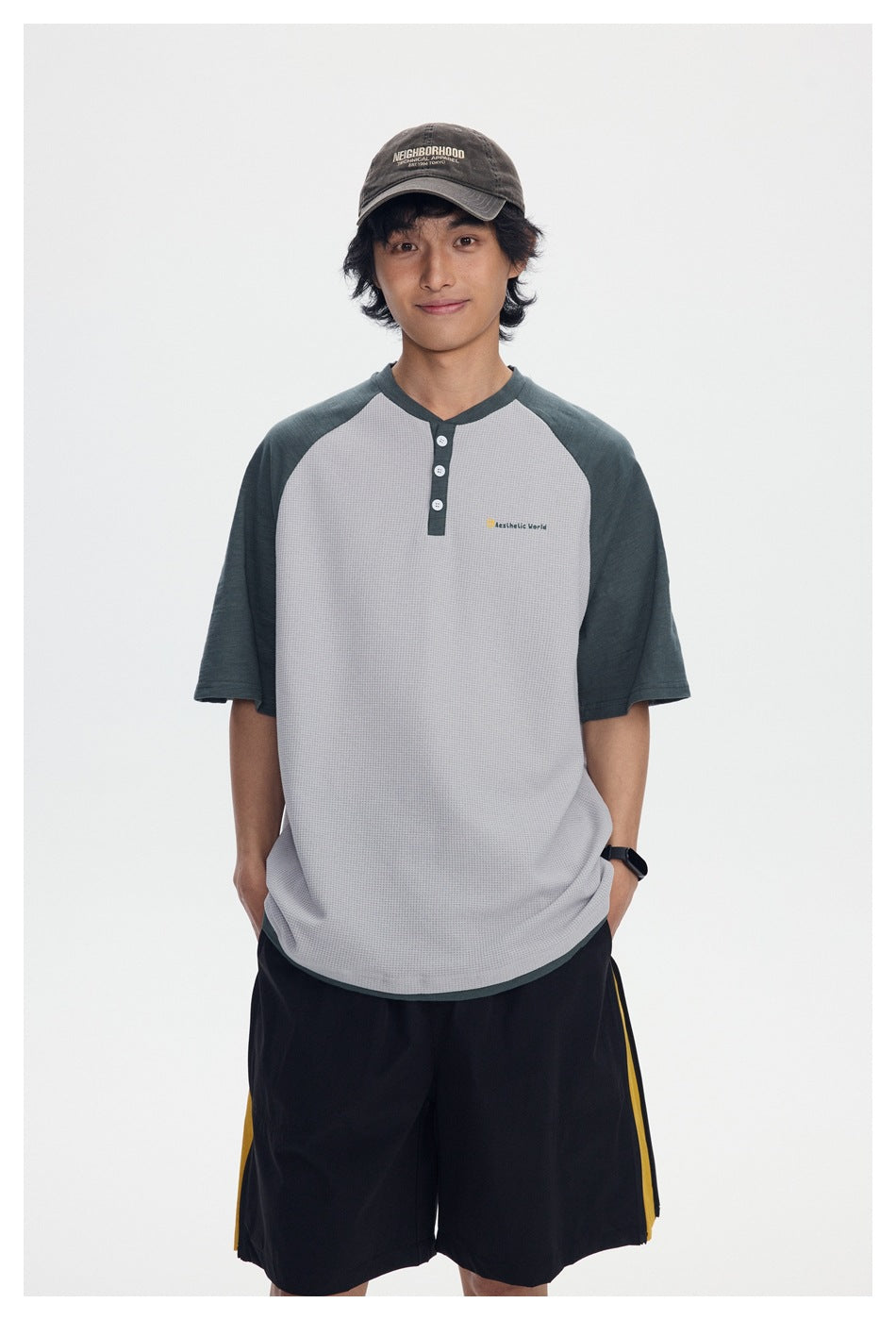 Front view of a model wearing a light gray waffle-knit henley with dark green raglan sleeves and black shorts with yellow