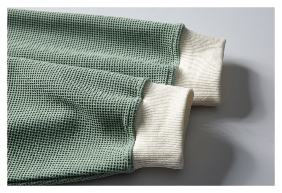 Close-up of two ivory ribbed cuffs on the sleeves of a sage-green textured shirt.