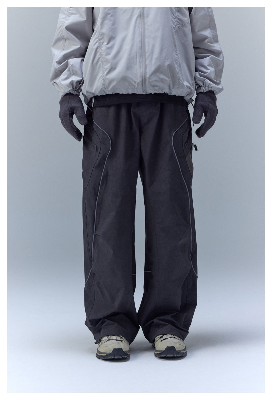 Front view of loose black cargo pants with curved piping, worn with a light gray jacket.