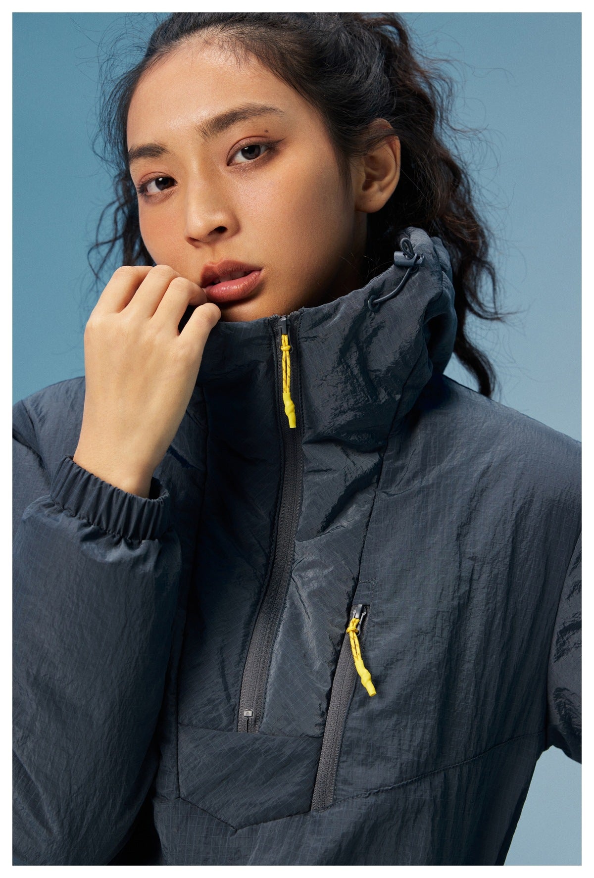 Close-up of a dark charcoal hooded jacket with a high collar and yellow zipper pulls.