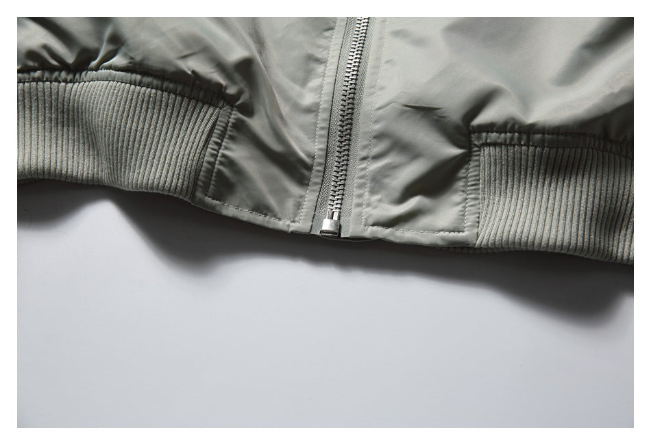Close-up of the pale gray-green jacket hem with ribbed trim and the bottom of its center zipper.