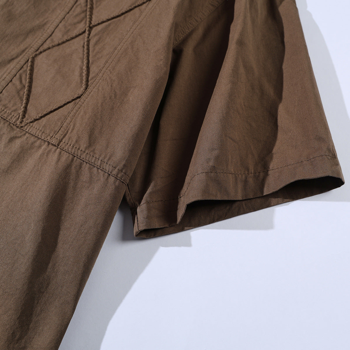 Close-up of the brown shirt's short sleeve, hem stitching, and geometric stitched panel.