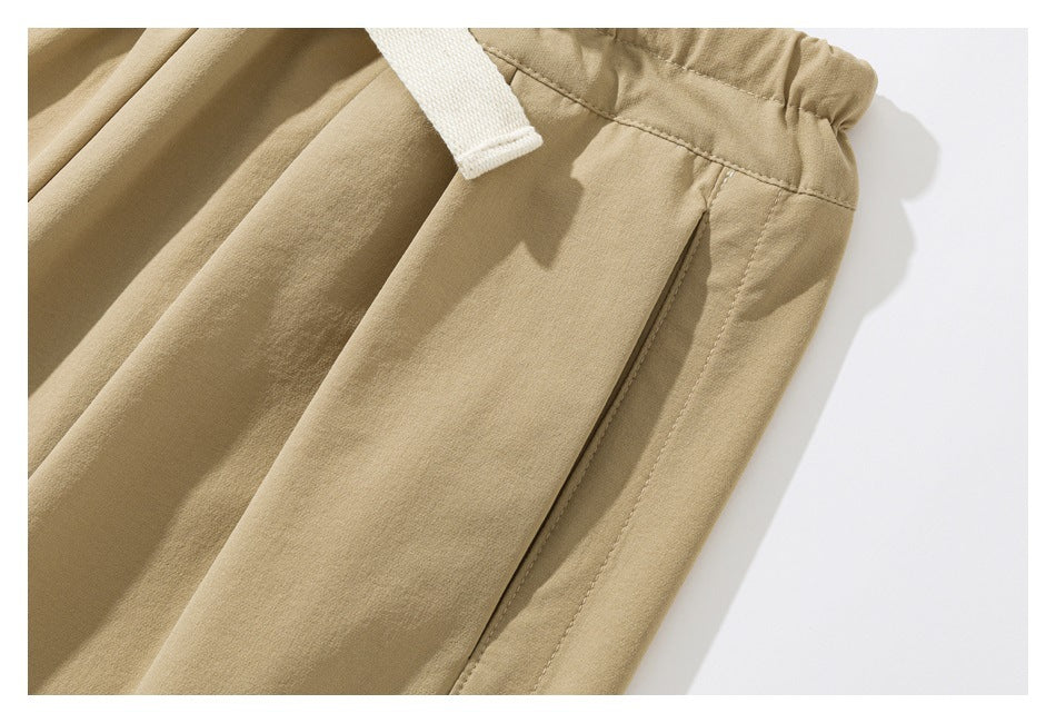 Close-up of tan pants showing a side pocket, elastic waistband, and part of a white drawstring.