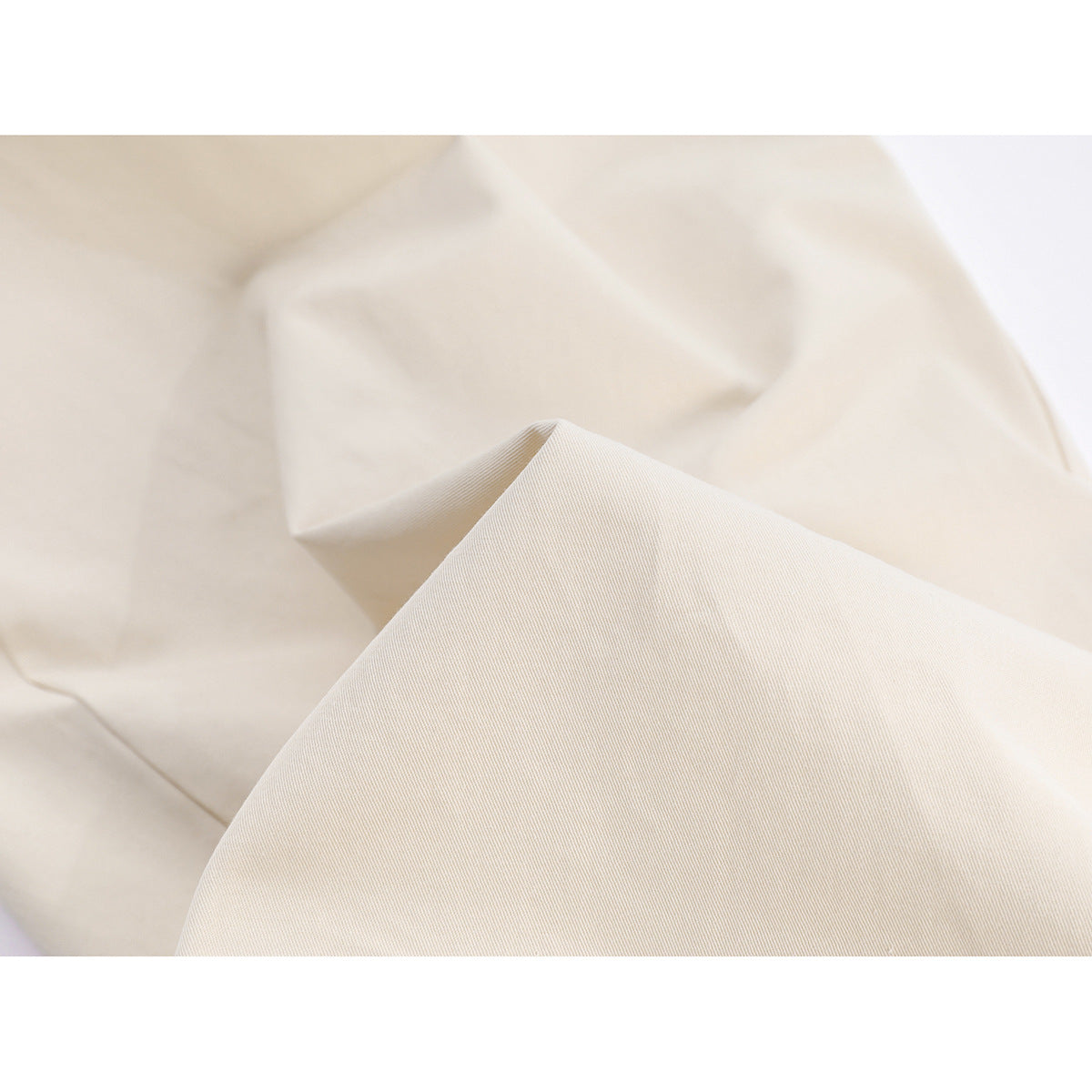 Close-up of ivory trouser fabric draped to show its fine diagonal weave and surface texture.