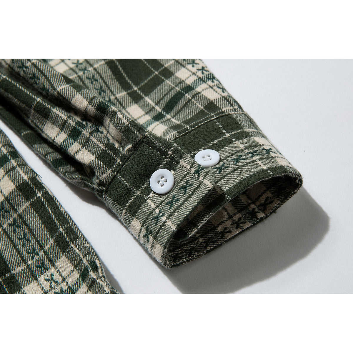 Close-up of a buttoned cuff on a dark green and cream plaid shirt.
