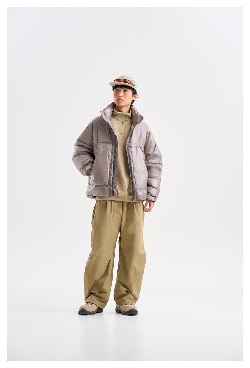 Model wearing a light gray puffer jacket with a high collar, paired with a beige top and loose khaki trousers.