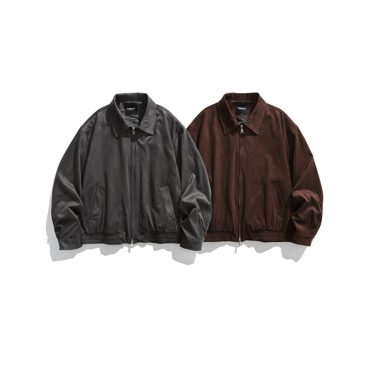 Front view of two zip-up jackets with pointed collars and gathered hems, in charcoal gray and dark brown.