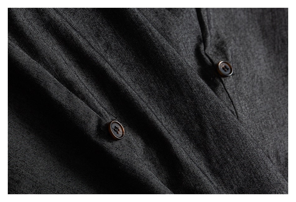 Close-up of dark charcoal trousers showing two brown buttons and diagonal seams.