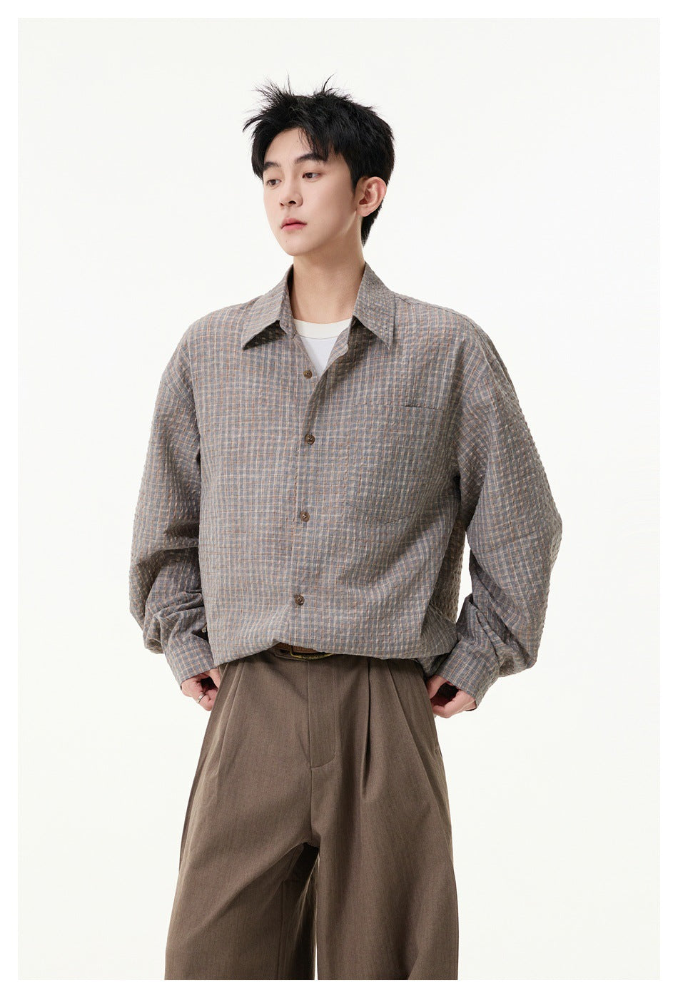 Model wearing a loose gray-brown checked button-up shirt with a chest pocket and brown trousers.