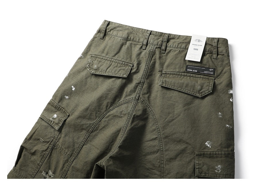 Partial back view of olive cargo trousers with flap pockets, belt loops, distressed marks, and a hangtag.
