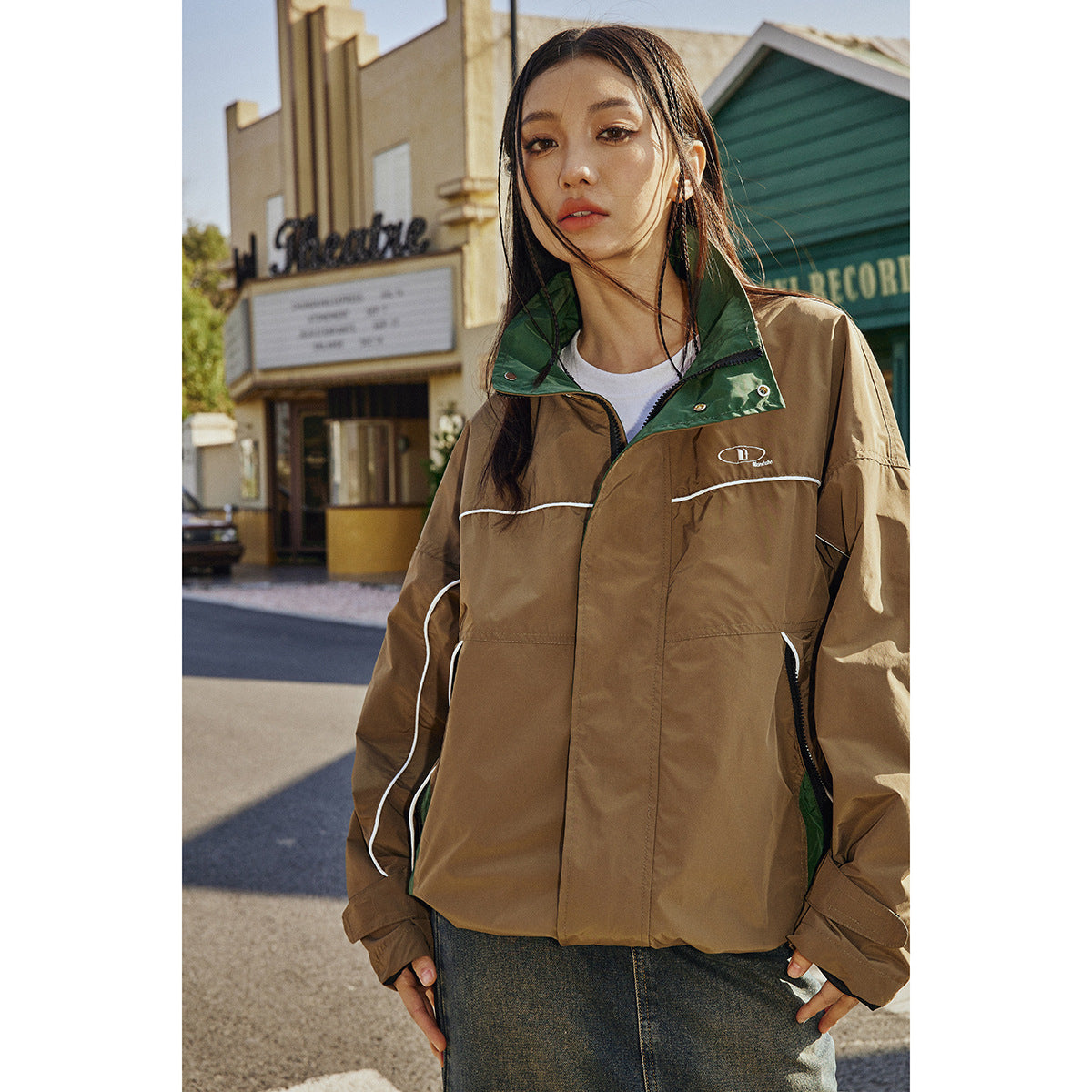 Model wearing a brown oversized zip jacket with a dark green collar and white piping, shown from the front.