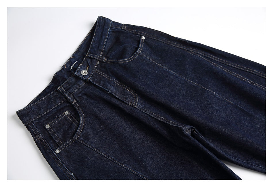 Angled close view of dark indigo jeans showing the waistband, front pockets, coin pocket and tan contrast stitching.