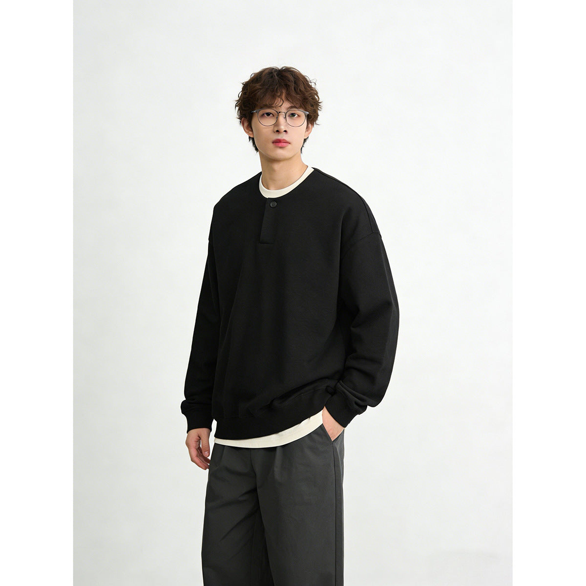 Model wearing a black oversized sweatshirt with a short button placket and cream layer underneath.
