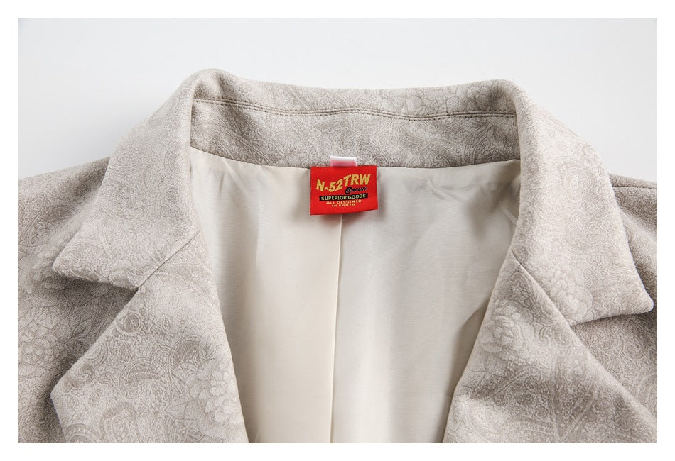 Close-up of a pale beige paisley blazer collar, cream lining, and red sewn-in neck label.
