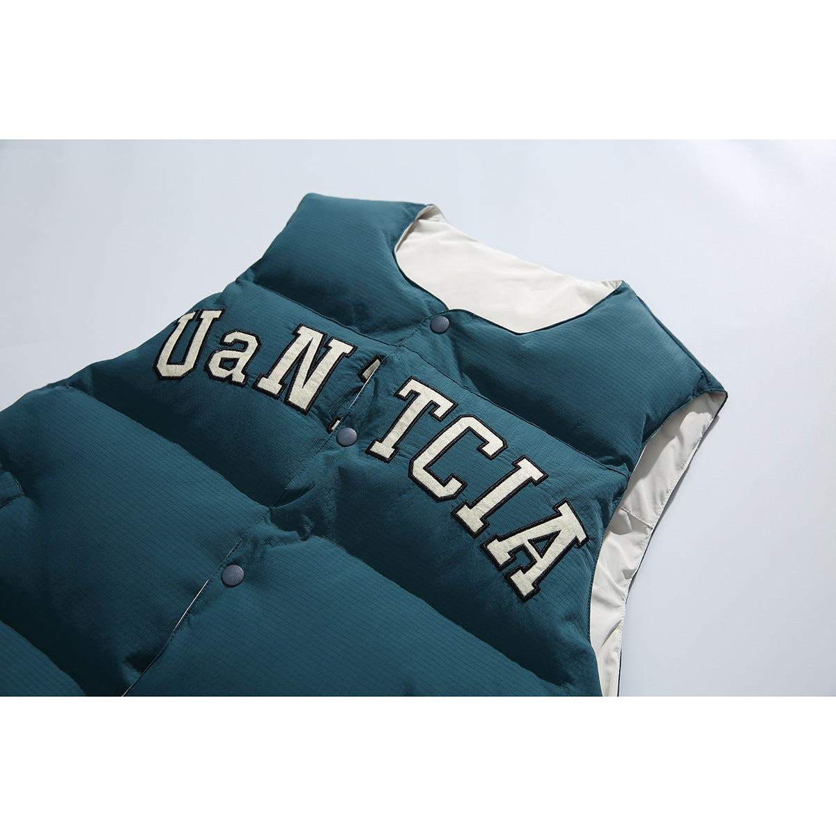 Close-up of a dark teal padded vest with snap buttons and large cream, black-outlined lettering across the chest.