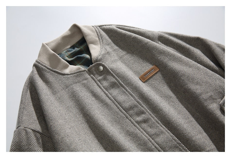 Close-up of a gray herringbone jacket with a beige ribbed collar, snap closure, plaid lining, and small sewn patch.