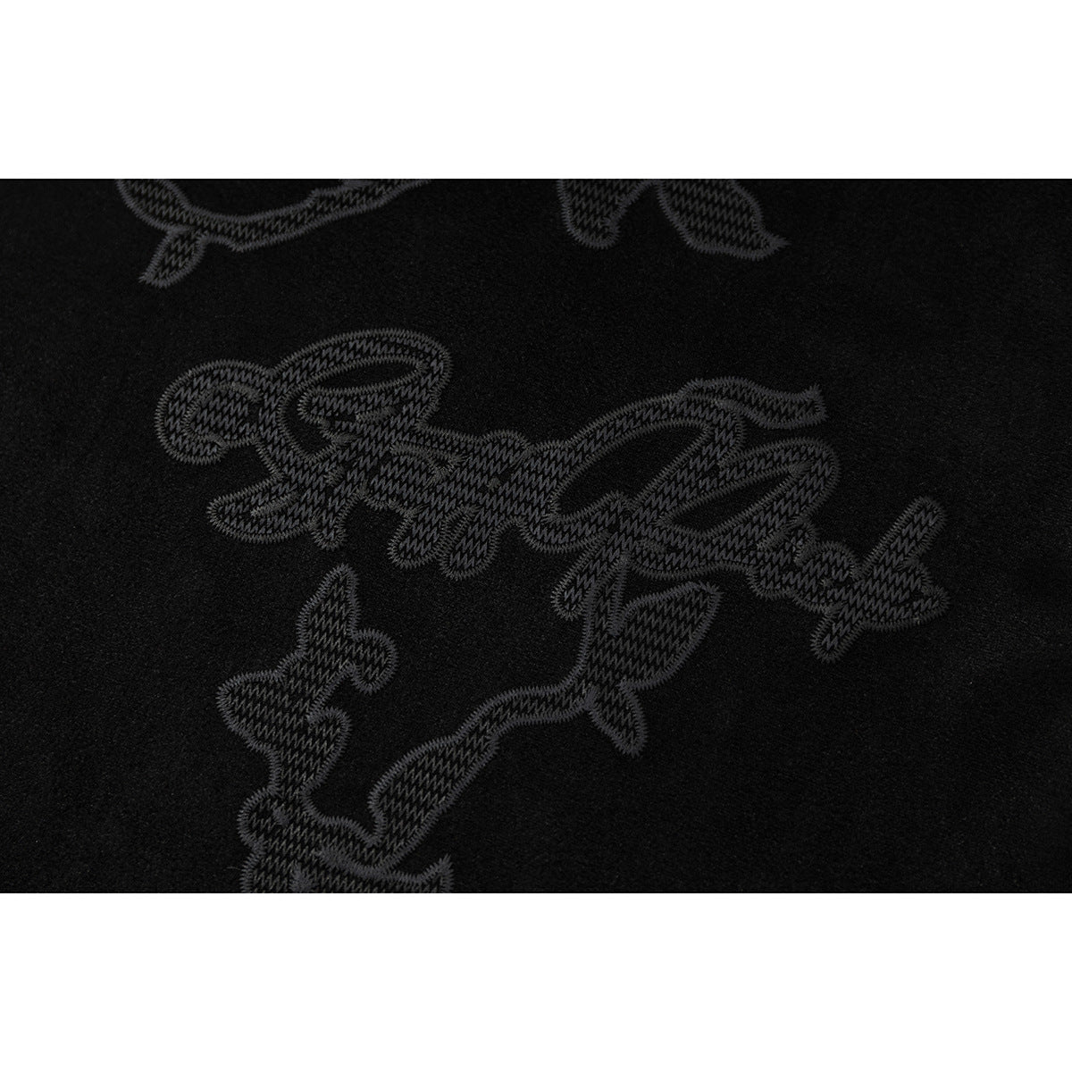 Close-up of dark embroidered script and abstract motifs on black fabric.