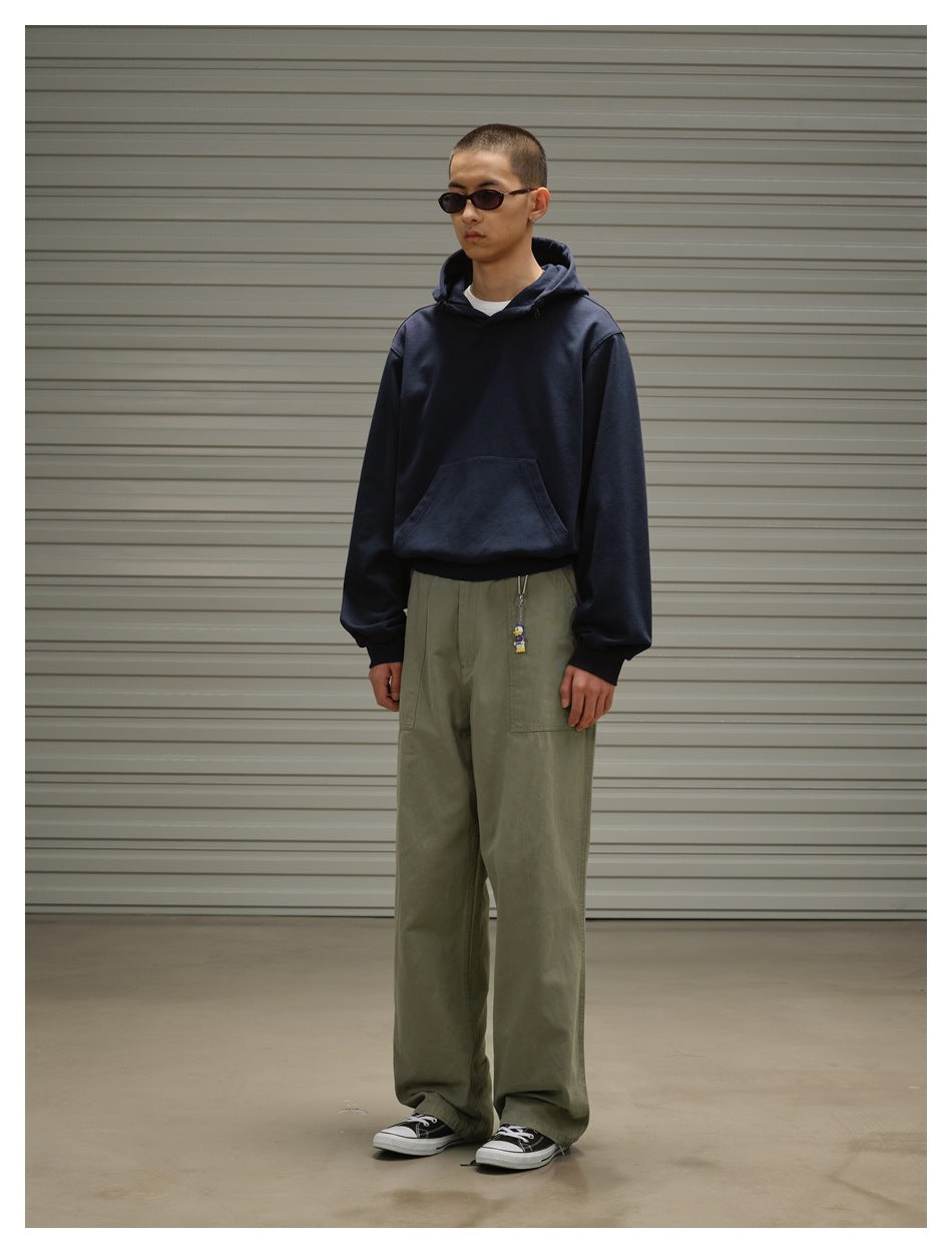 Model in a dark navy pullover hoodie with a kangaroo pocket and loose olive trousers, shown at a three-quarter angle.