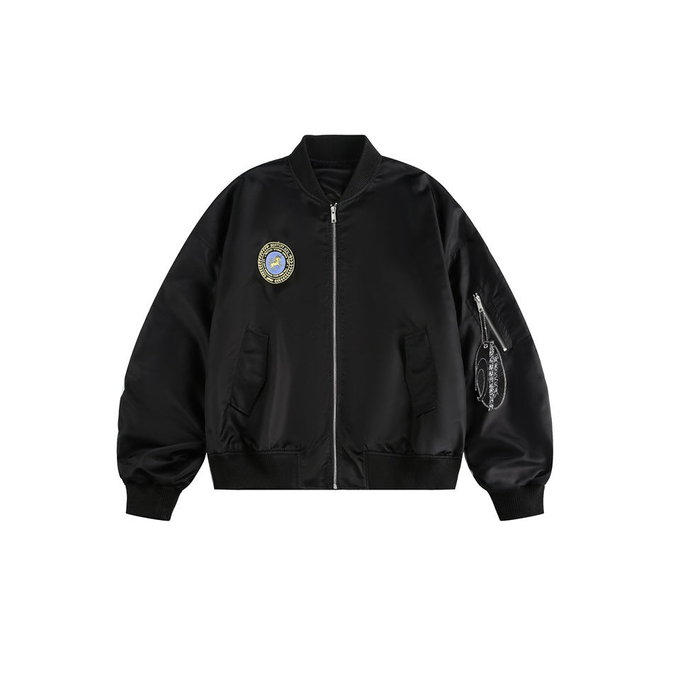 Black bomber jacket flat lay with front zipper, ribbed trim, round chest patch and zippered sleeve pocket