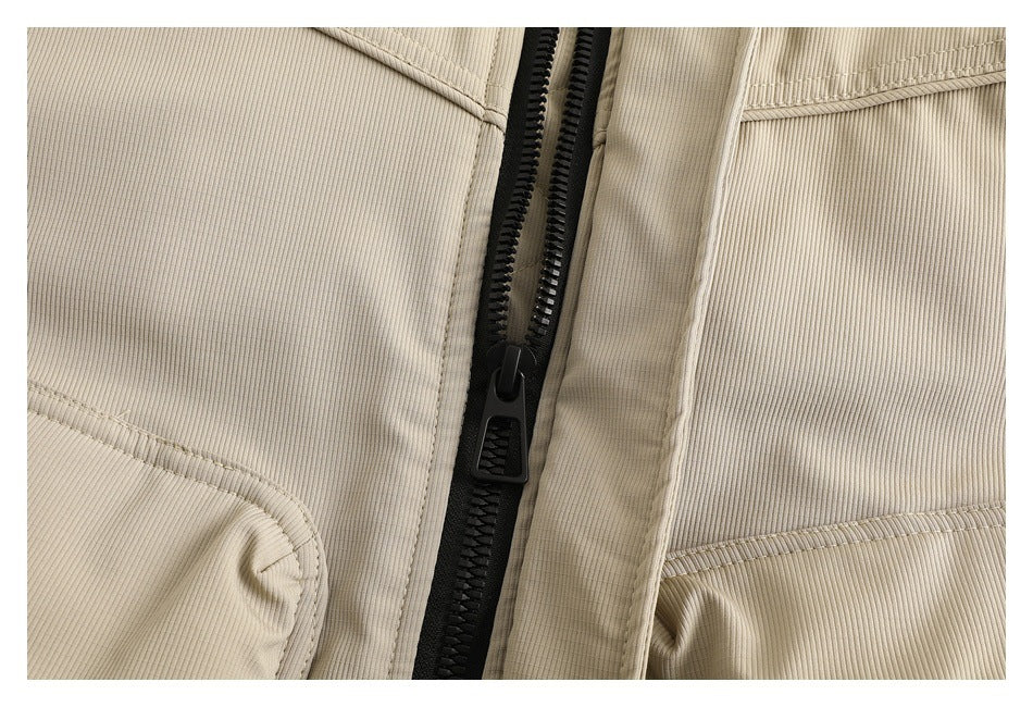 Close-up of a beige jacket with a black front zipper, stitched panels, and a fine ribbed texture.