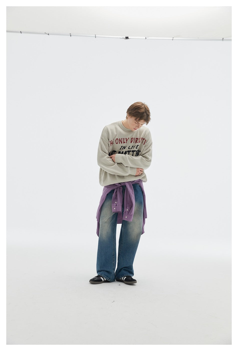Model wearing a light gray slogan sweatshirt, wide-leg blue jeans, and a purple shirt tied at the waist.