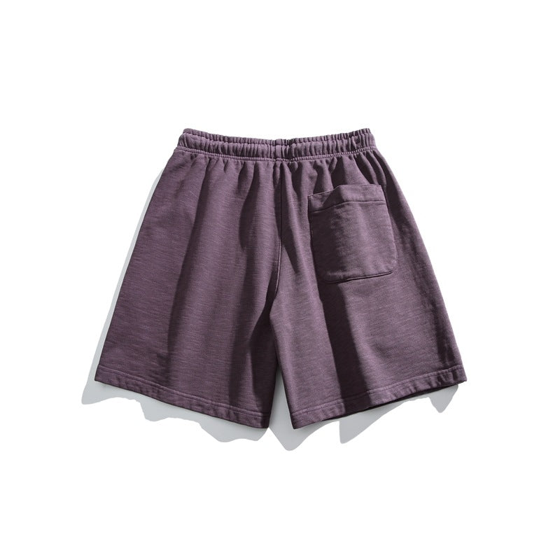 Back view of muted plum-purple shorts with an elastic waistband and a single patch pocket.