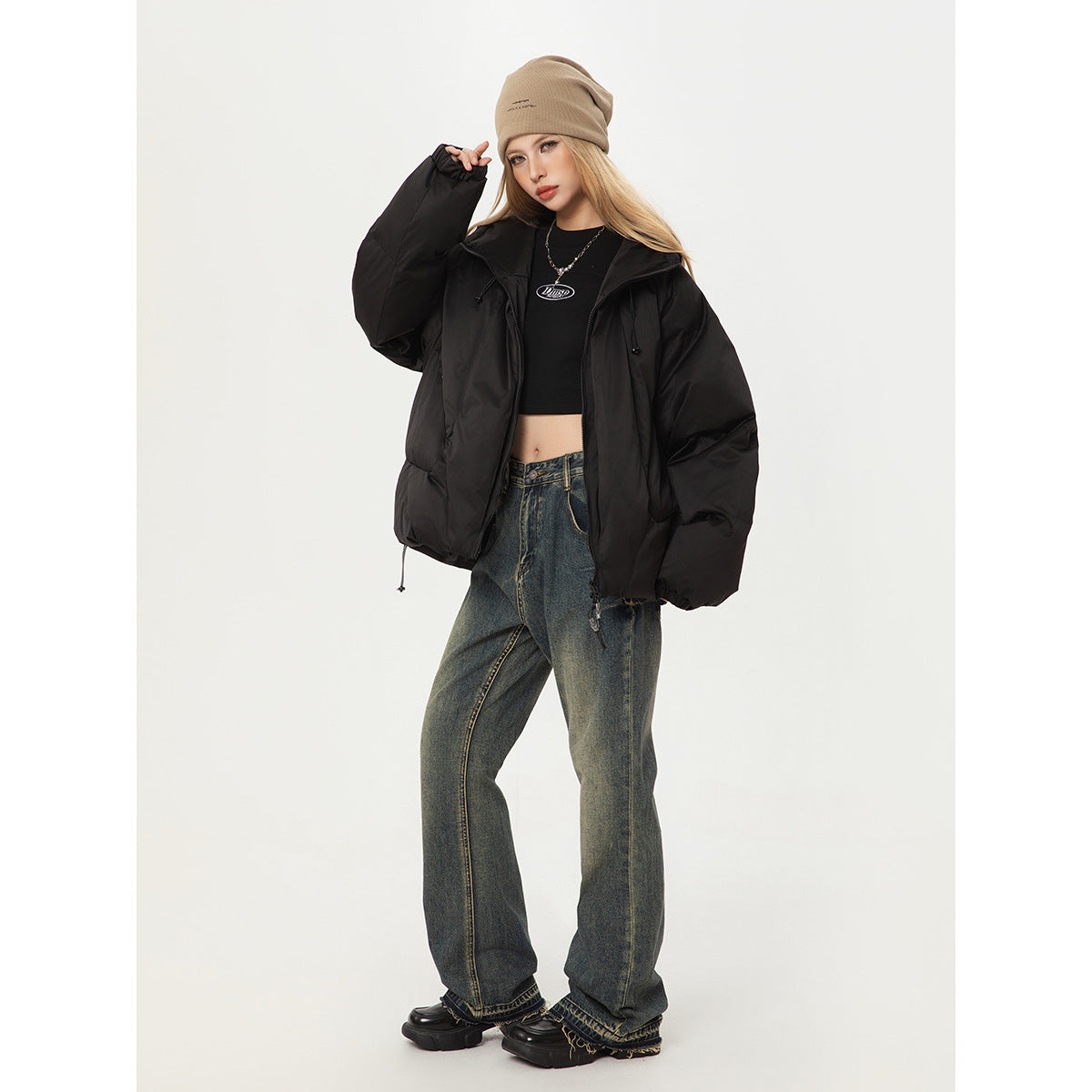 Model wearing an oversized black hooded puffer jacket with a beige beanie, black crop top and loose dark jeans.