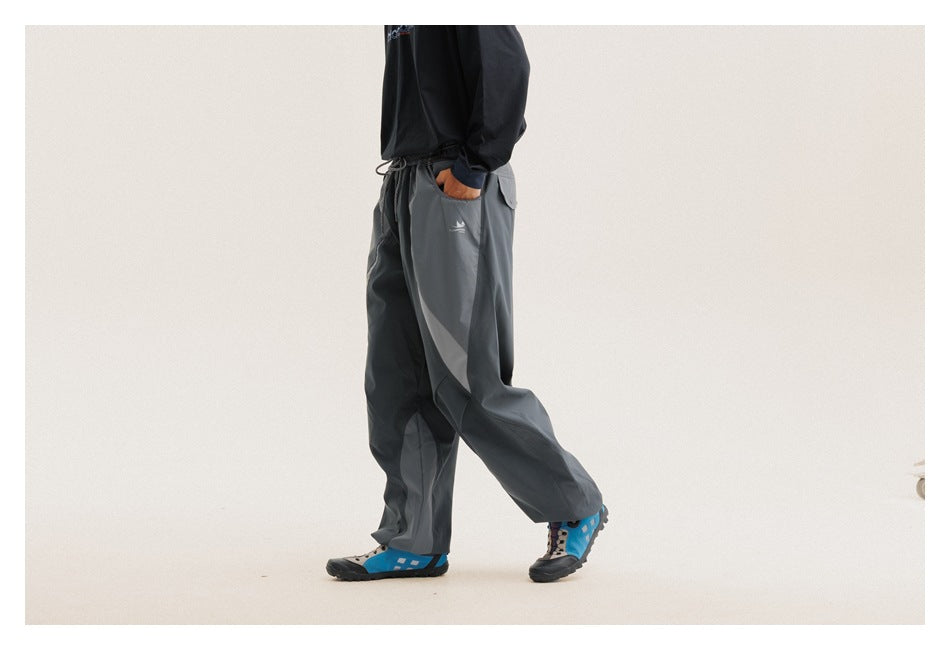 Side view of a model wearing loose charcoal-gray pants with curved contrast panels, a drawstring waist and side pockets.