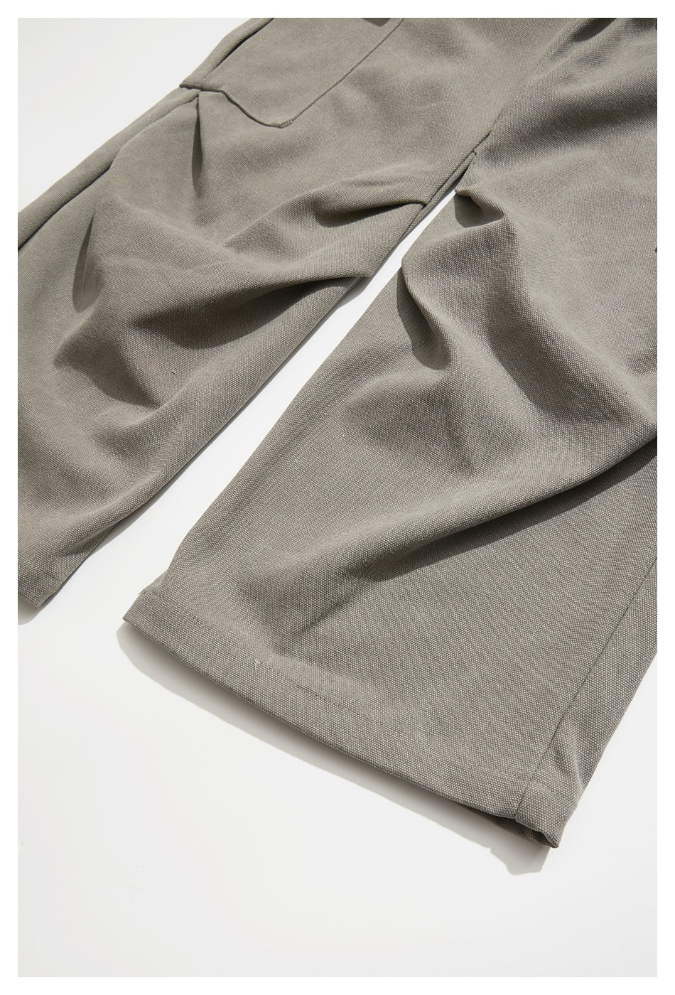Partial flat lay of taupe-gray trousers showing the legs and stitched hems.